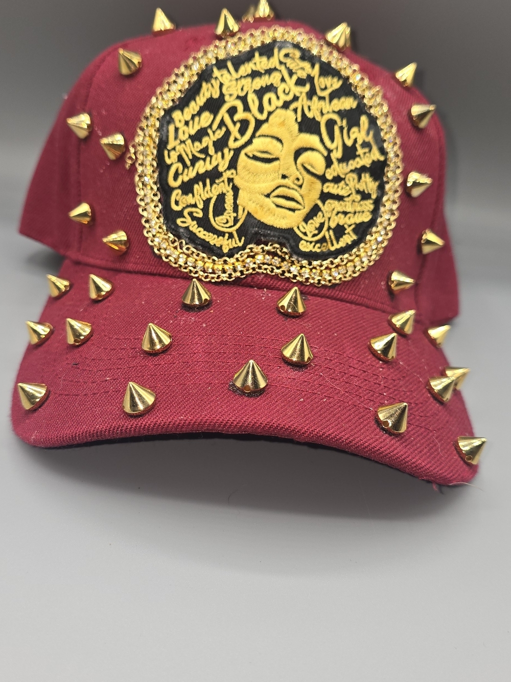 Gold-Studded Burgundy Cap with Embroidered Black Afro Motif